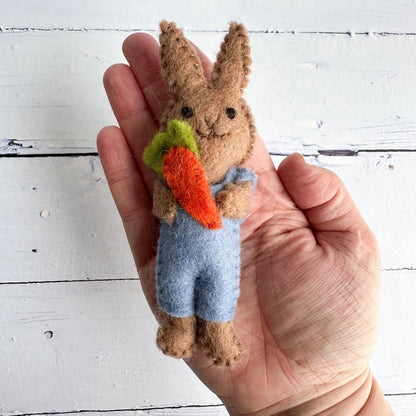 Small felt rabbit toy holding a carrot, held in a hand against a white wooden background