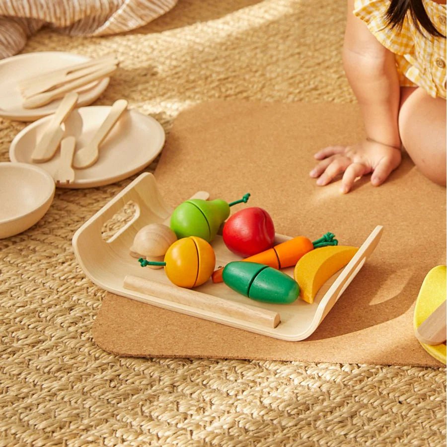Child playing with wooden toy fruits and vegetables on a mat
