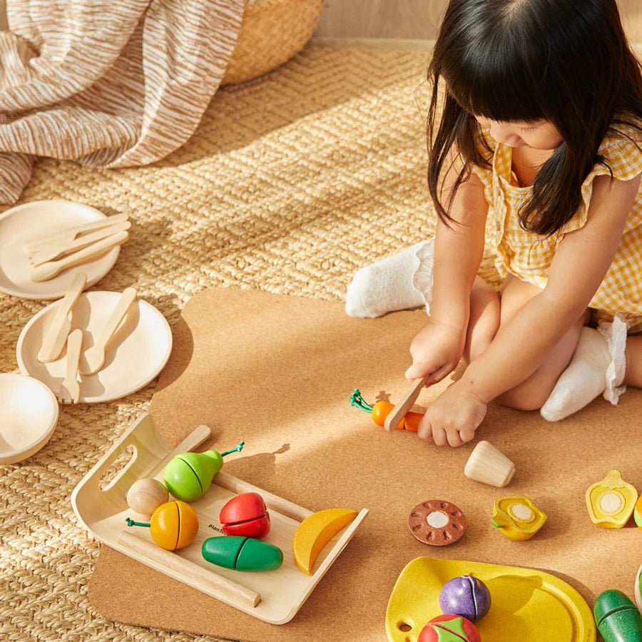 Child playing with colorful wooden fruits and veggies on a cork mat