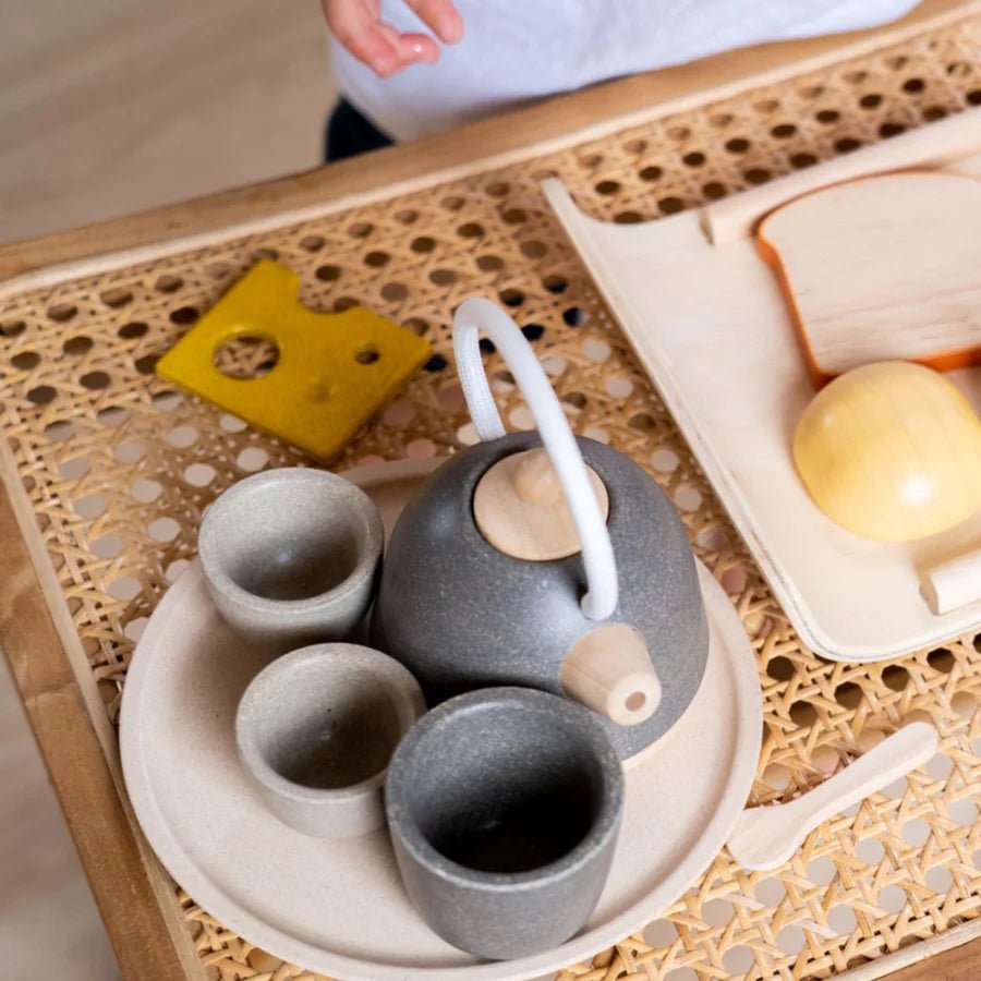Wooden play tea set on a wicker tray with play food and cutting board