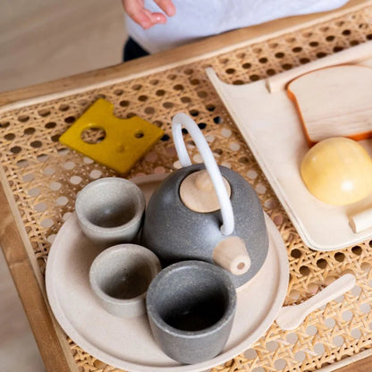 Wooden play tea set on a wicker tray with play food and cutting board