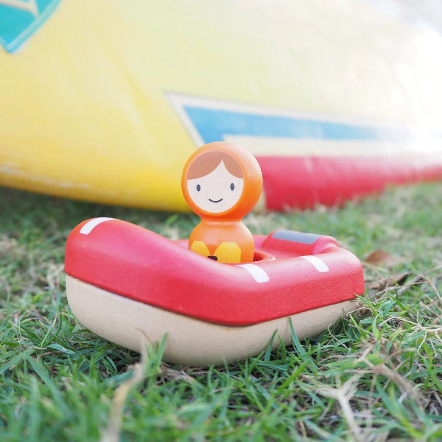 Small figurine in a red and white lifeboat on grass with colorful boats in the background