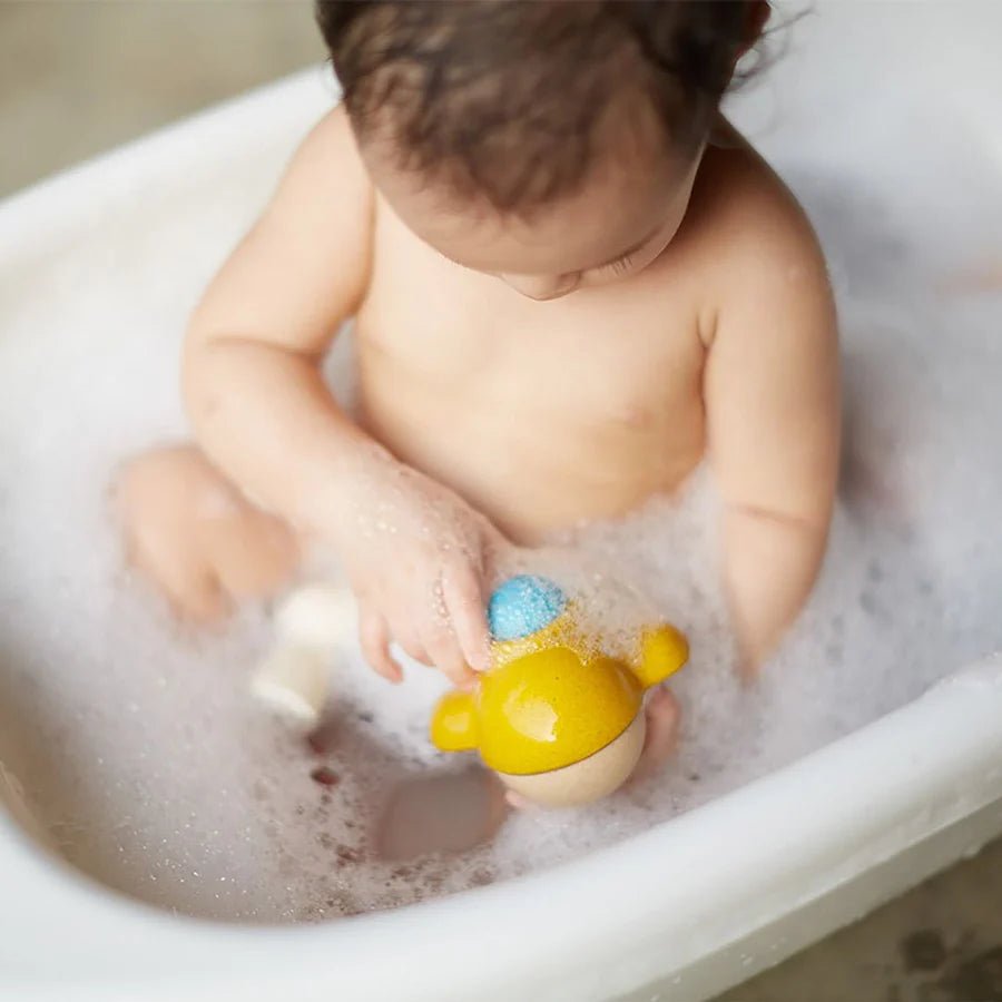Child playing with a yellow submarine bath toy in a bathtub filled with bubbles