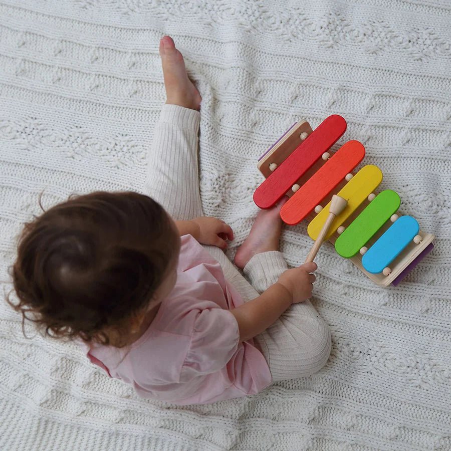 Child playing colorful xylophone on a knitted blanket