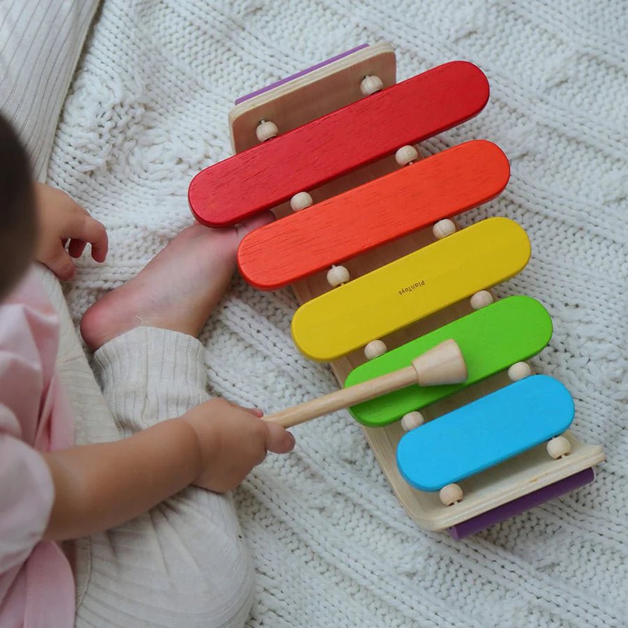 Child playing with a colorful wooden xylophone toy on a textured blanket