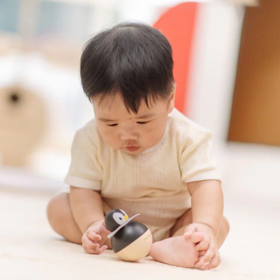 Baby playing with wooden penguin wobbling toy on a carpeted surface