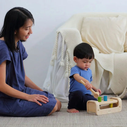 An adult supervises a small child playing with a wooden peg board with a white couch in the background