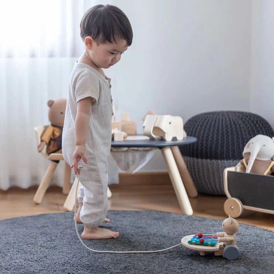 Child playing with a wooden bear pull toy on a carpeted floor in a room with furniture and toys.