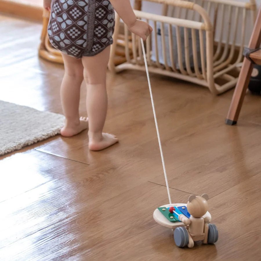 Child pulling a wooden toy bear on a wooden floor