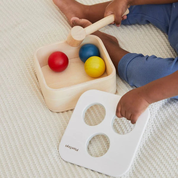 Child playing with colorful wooden balls and a mallet on a textured surface