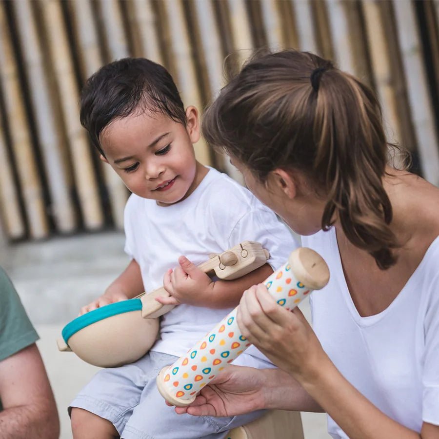 Adult and child playing with wooden toy instruments outdoors