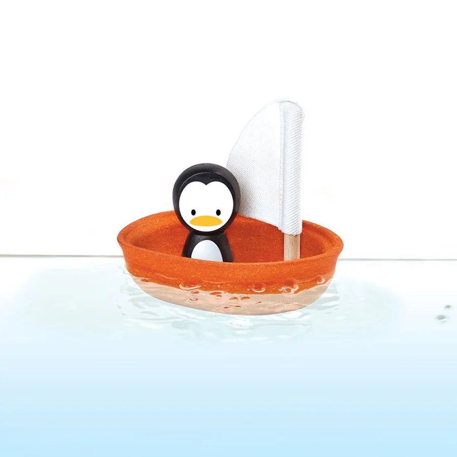 Penguin toy in an orange boat with a white sail on a light blue background