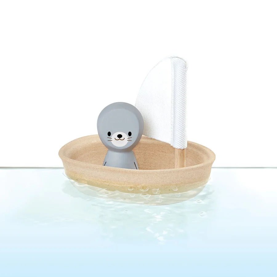 Toy seal in a small boat with a white sail on a light blue background