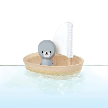 Toy seal in a small boat with a white sail on a light blue background