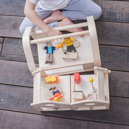 Child playing with a wooden dollhouse and dolls on a wooden surface