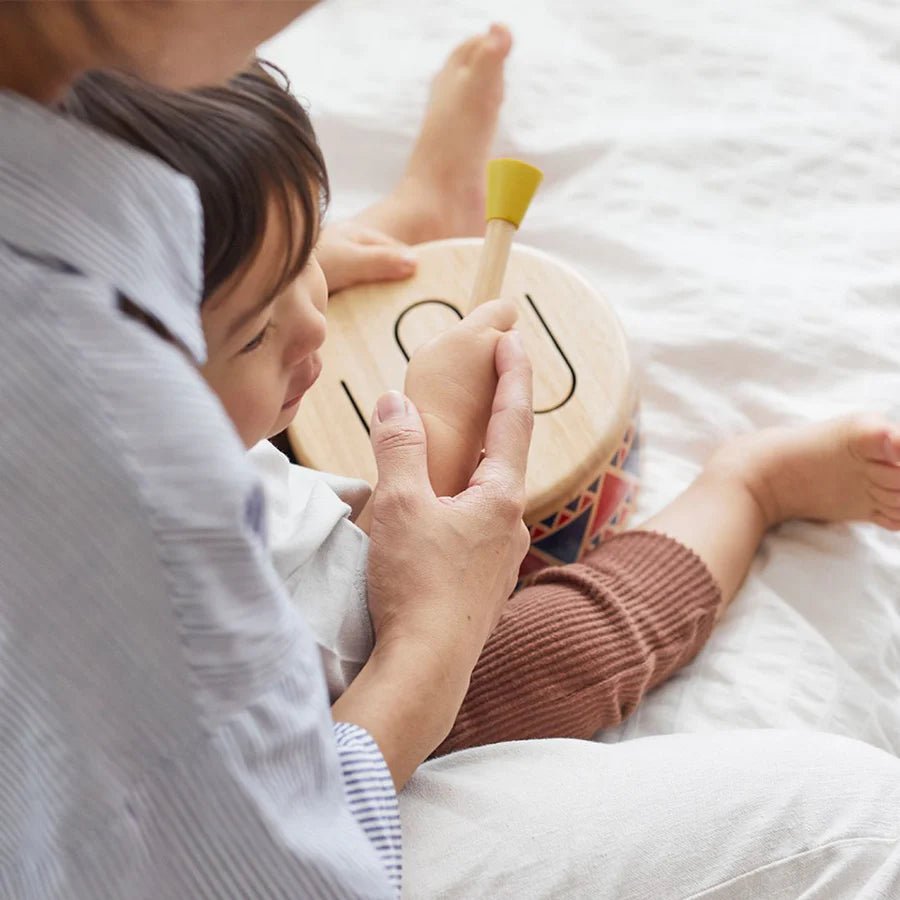 Parent and child playing with a small drum on a bed