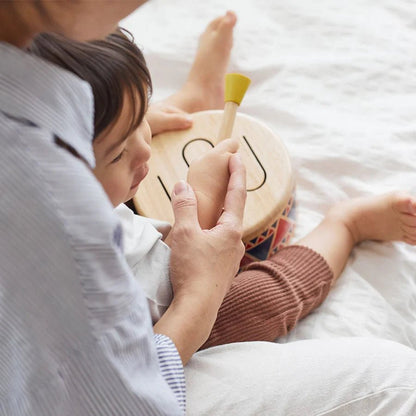 Parent and child playing with a small drum on a bed