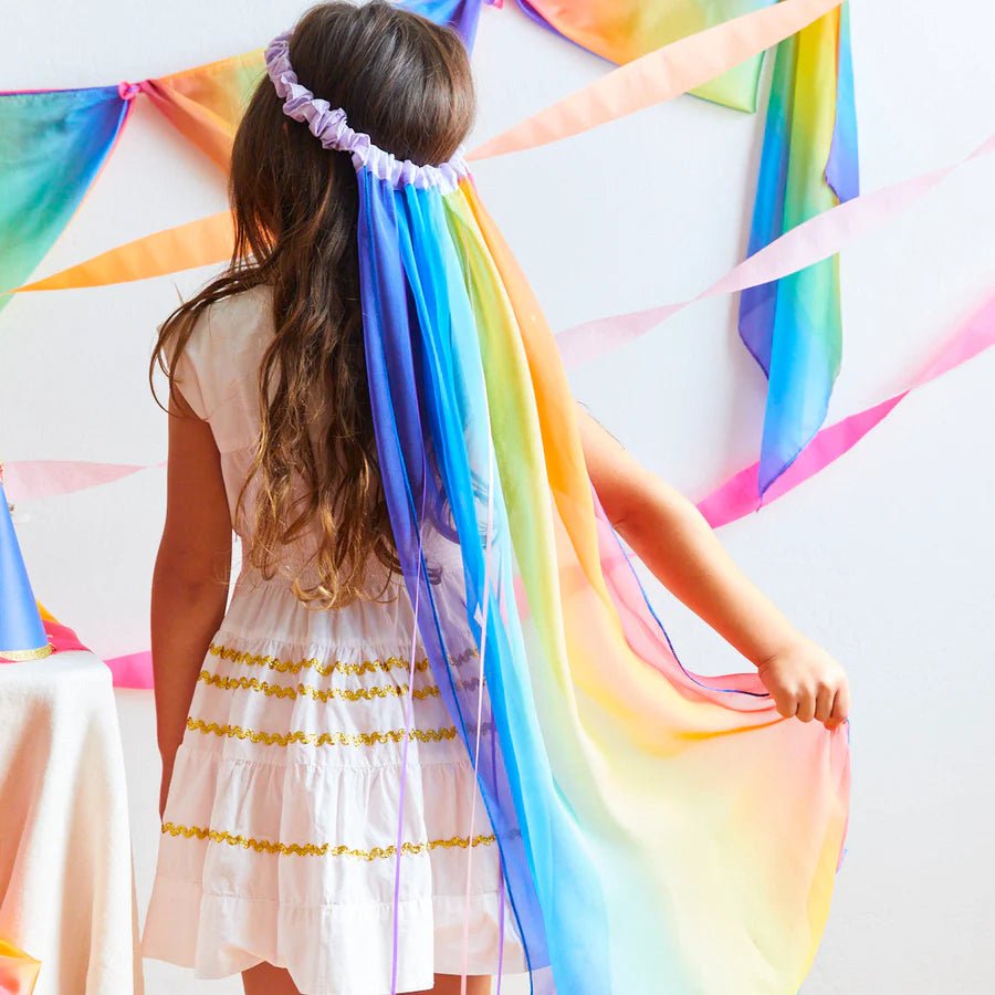 Rear view of a child wearing a long rainbow veil with silk decorations on the walls