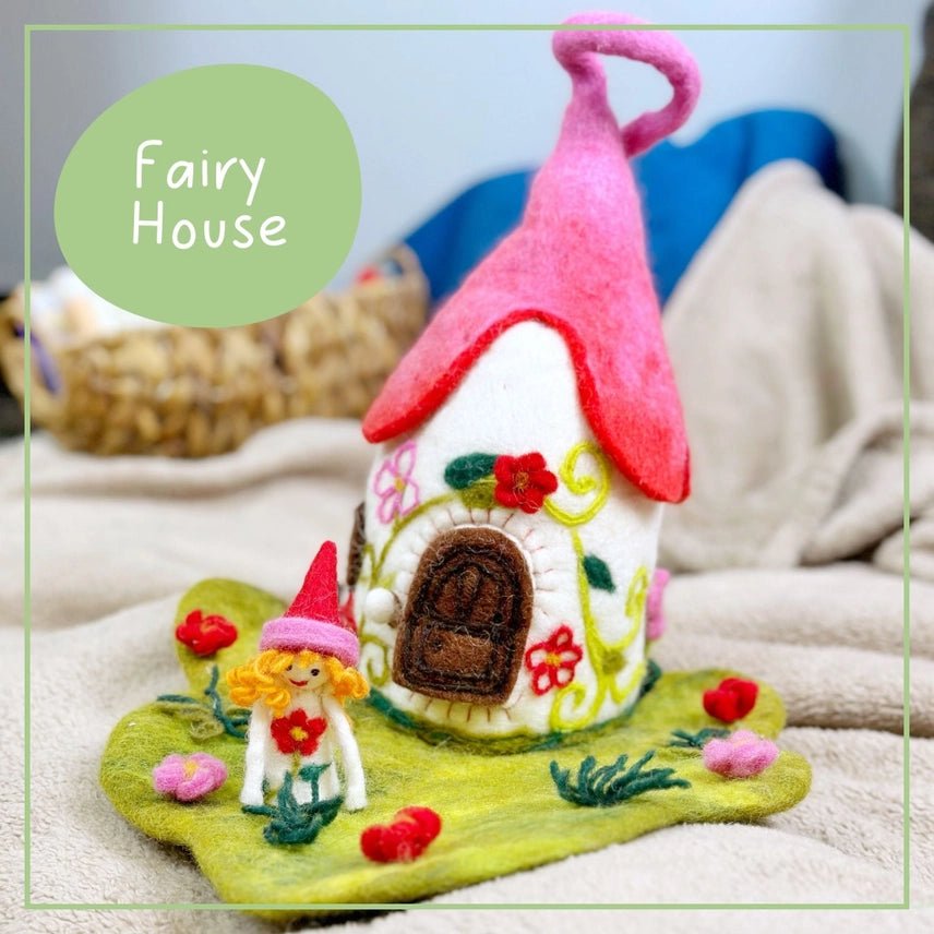 Felt fairy house with a pink roof and small fairy figure on a soft surface.