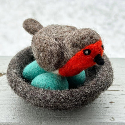 Felted toy robin bird in a nest on a wooden surface