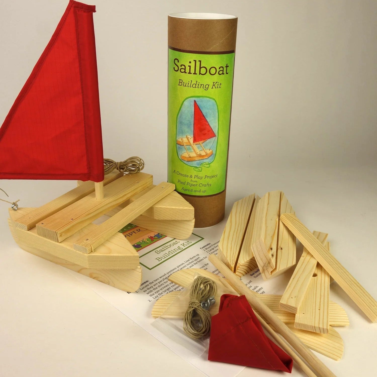 Wooden sailboat building kit with red sail and packaging on a white background