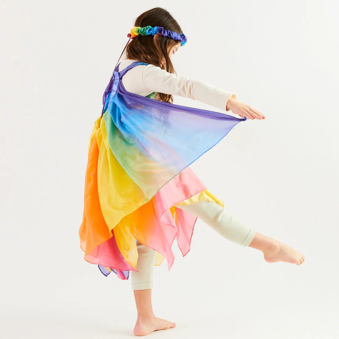Child wearing rainbow garland, rainbow wings, and rainbow skirt on a light background