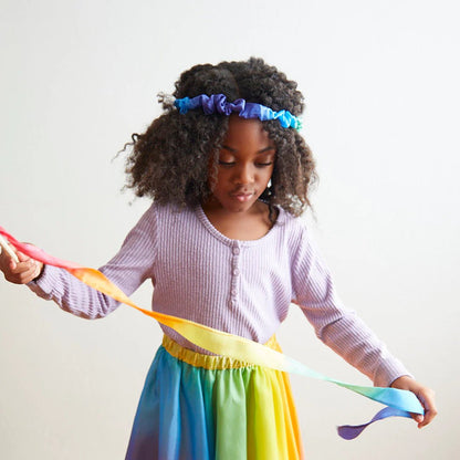 Child wearing a rainbow garland and skirt while holding rainbow streamer