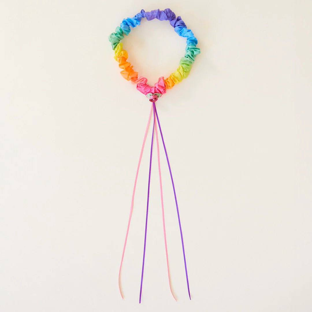Rainbow colored garland with pink and purple ribbons attached on a light background