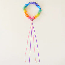Rainbow colored garland with pink and purple ribbons attached on a light background