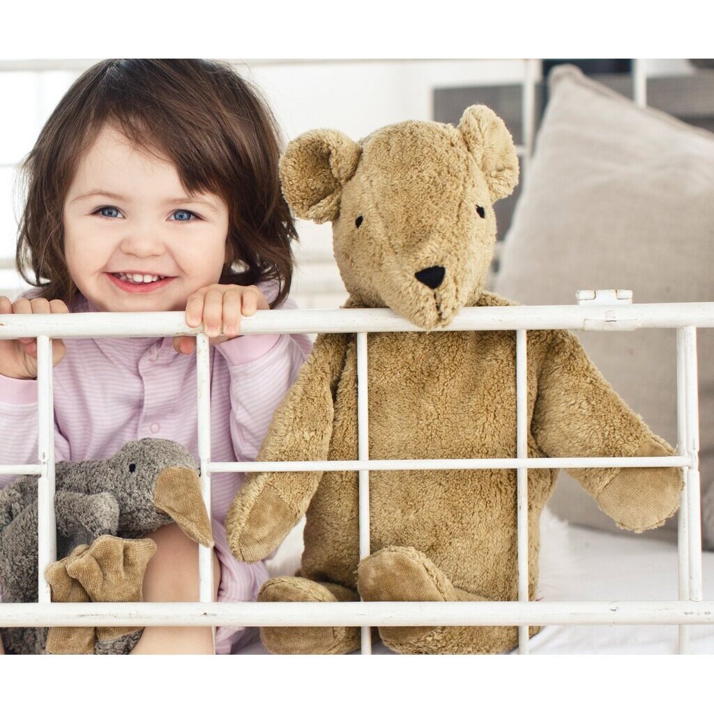 Child with senger teddy bear behind a white crib rail