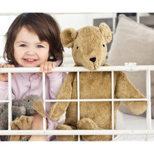 Child with senger teddy bear behind a white crib rail
