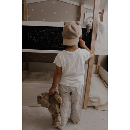 Child in a bedroom holding a senger cuddly teddy bear, standing in front of a bunk bed with a chalkboard wall.