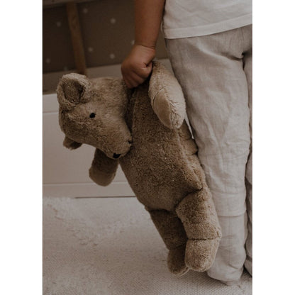 Child holding a Senger beige teddy bear in a room with a neutral color palette.