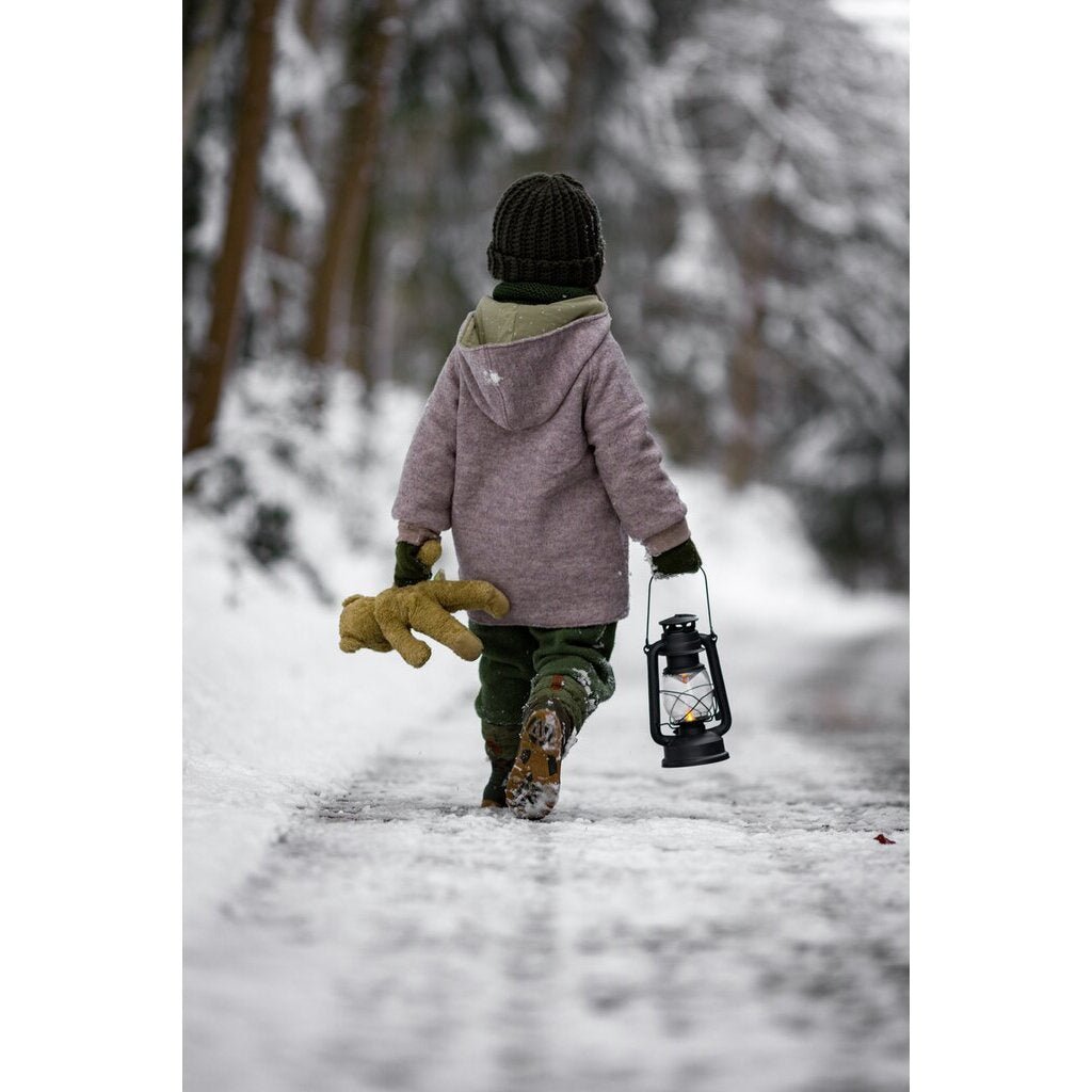 Person walking in a snowy forest with a lantern and Senger beige teddy bear 