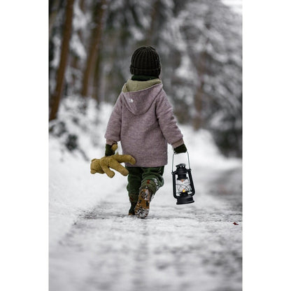 Person walking in a snowy forest with a lantern and Senger beige teddy bear 
