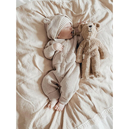 Baby in knitted outfit lying on a soft surface with a Senger beige teddy bear 
