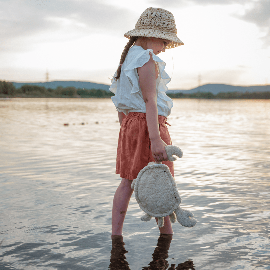 Young girl holding a plush crab by a lake with a cloudy sky.