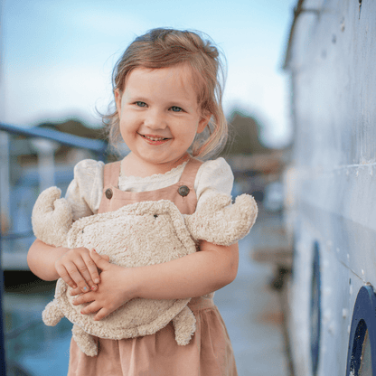 Young girl holding a stuffed crab outdoors with a blurred background