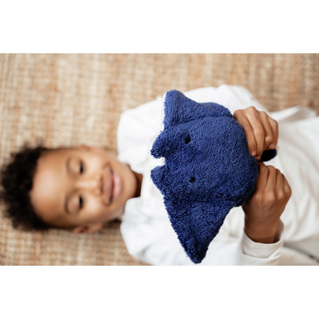 Child holding a blue manta ray stuffed animal on a woven surface