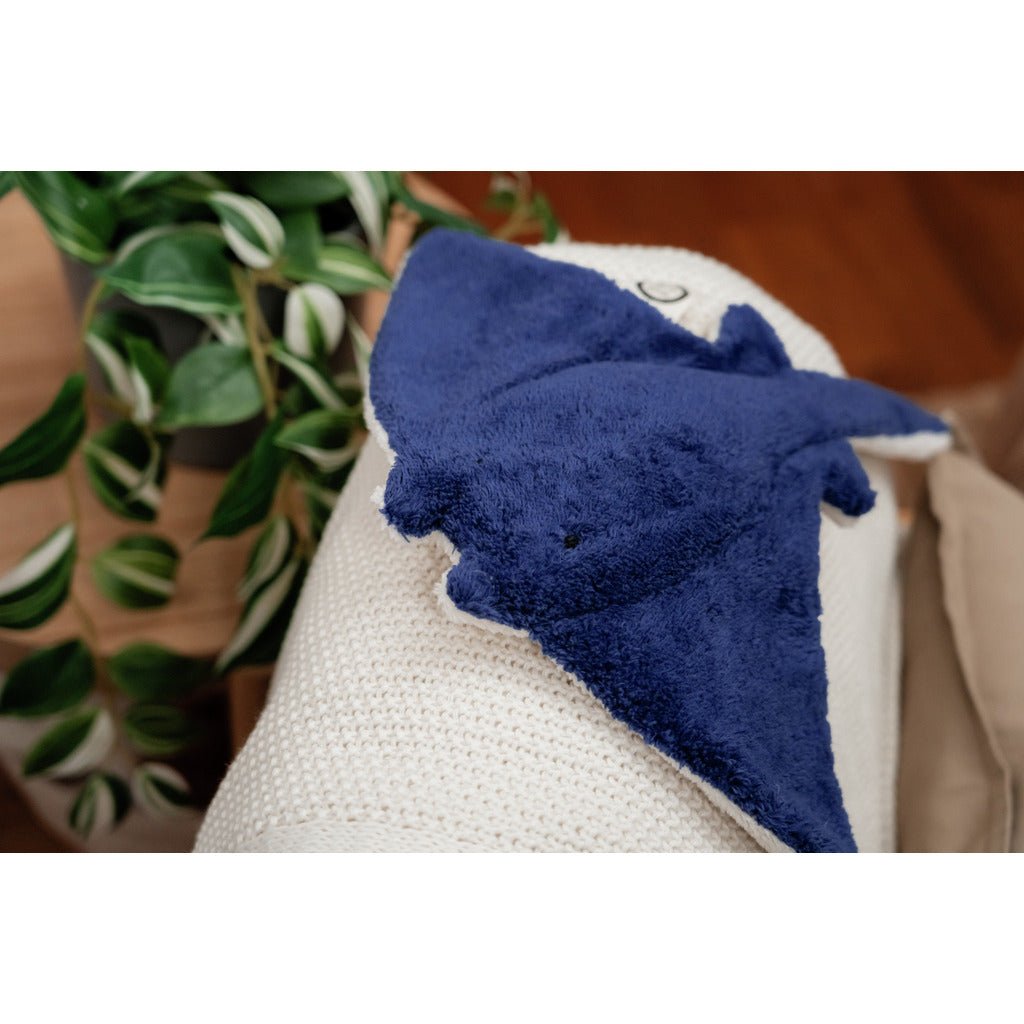 Blue manta ray stuffed animal on a white blanket with a plant in the background