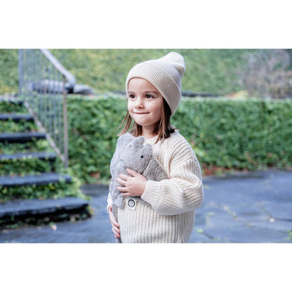 Child wearing a knit sweater and hat, holding a plush manta ray outdoors.