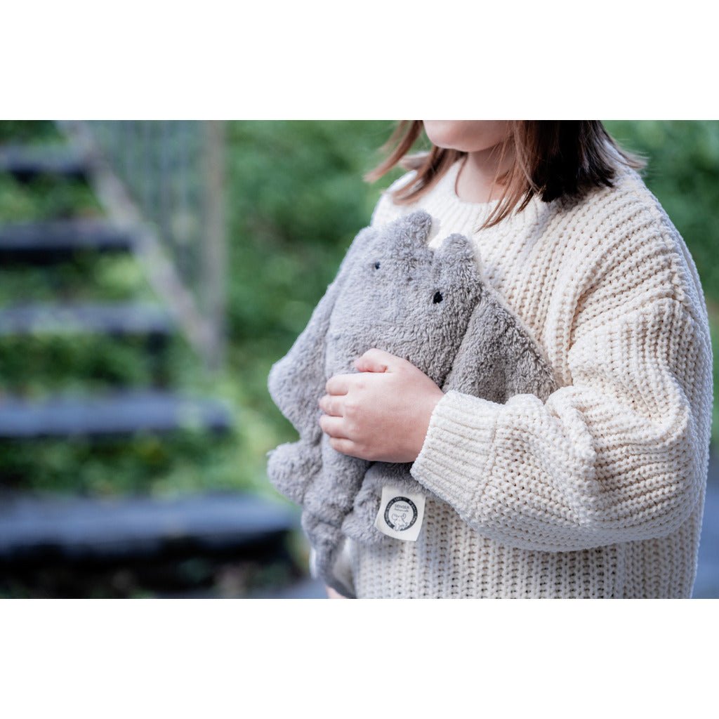 Child wearing a beige knit sweater holding a gray plush manta ray outdoors.