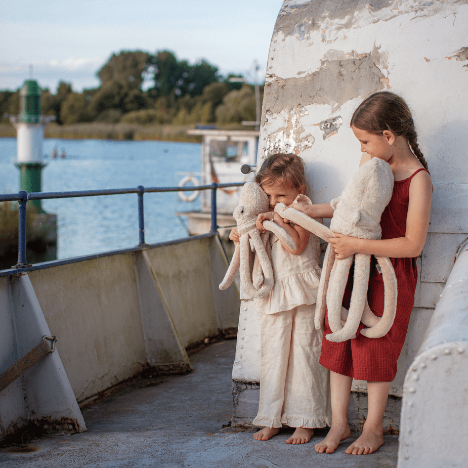 Two children holding octopus stuffed animals on a boat deck with water and sky in the background