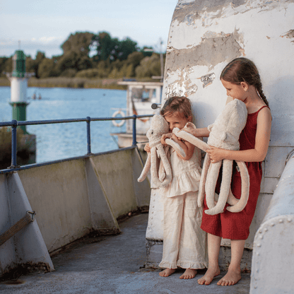 Two children holding octopus stuffed animals on a boat deck with water and sky in the background