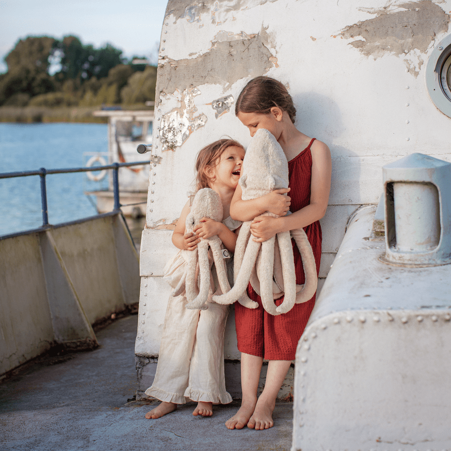 Two children holding a large white octopus stuffed animal on a boat deck by a body of water.