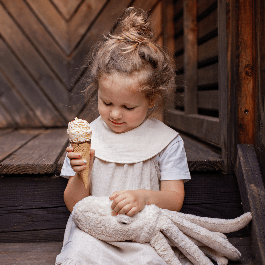 Child holding a ice cream cone and plush toy against a wooden background