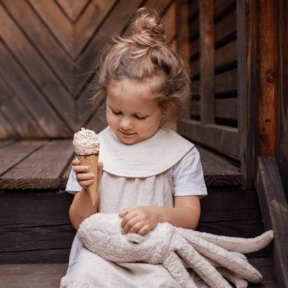 Child holding a ice cream cone and plush toy against a wooden background