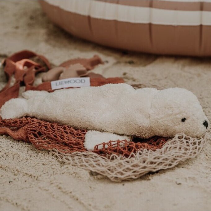 White plush seal laying on a net on a sandy surface