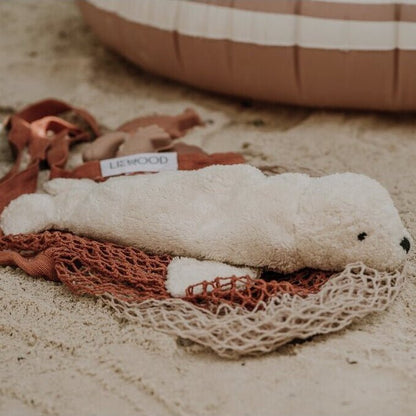 White plush seal laying on a net on a sandy surface