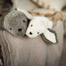 Two plush toy seals, one gray and one white, on a textured blanket with a blurred background.